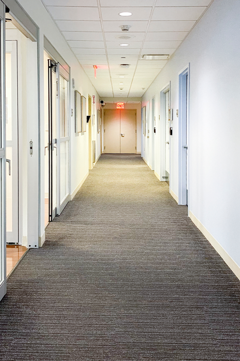 Empty office hallway with white walls, gray carpet, and doors along both sides
