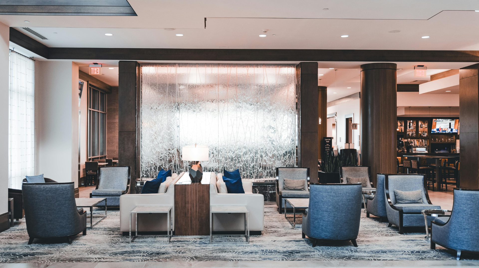 Modern hotel lobby with blue and gray lounge chairs, patterned carpet, and a large art wall