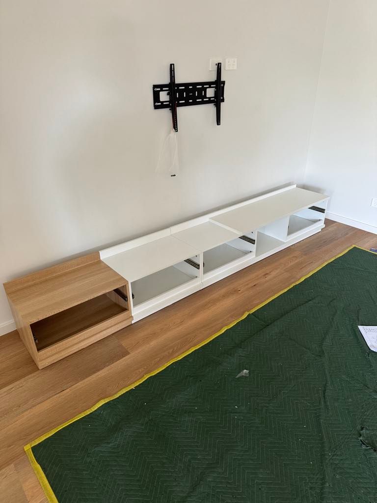 Wall-mounted TV bracket above a low white shelf and wooden bench in a room with green carpet.