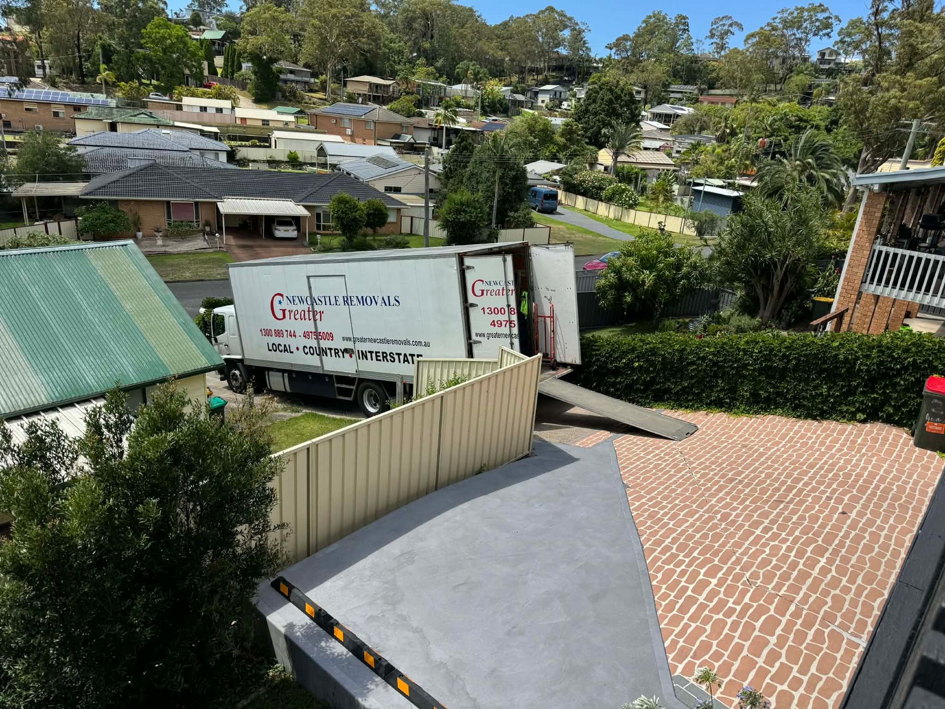 Truck parked near a brick driveway beside a hillside neighborhood and trees