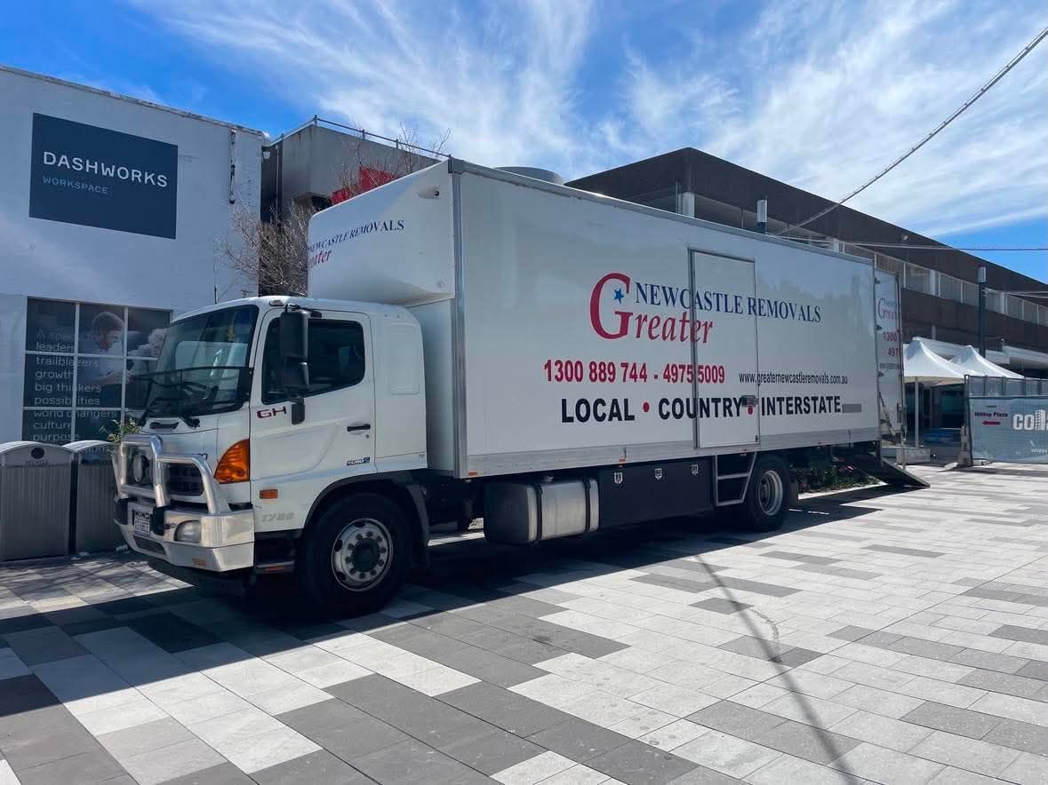 White delivery truck parked outside a building, with “Grocery” text on the side under a bright blue sky.