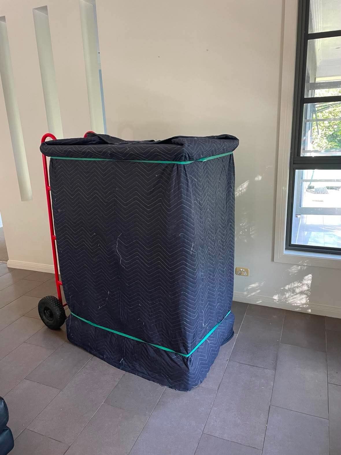 Black wheeled cart or hamper wrapped with green and red straps in a sunlit room