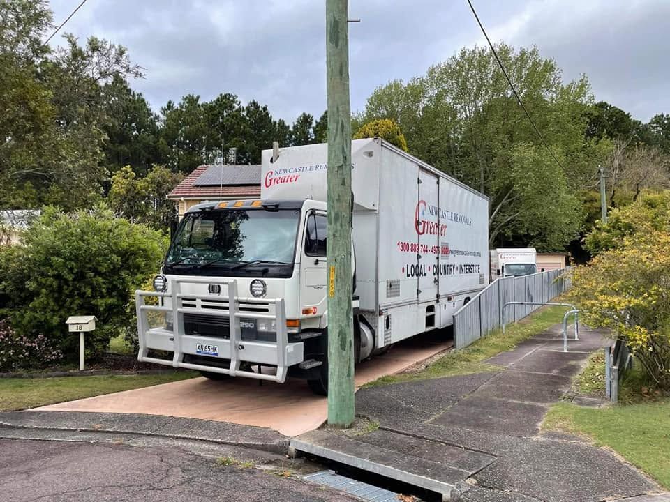 White moving truck parked on a narrow residential driveway beside a utility pole and fence.