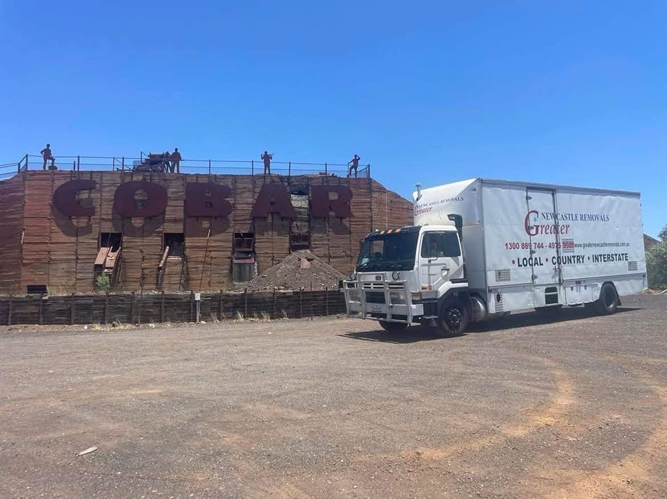 White delivery truck parked beside a weathered brick building under a clear blue sky.