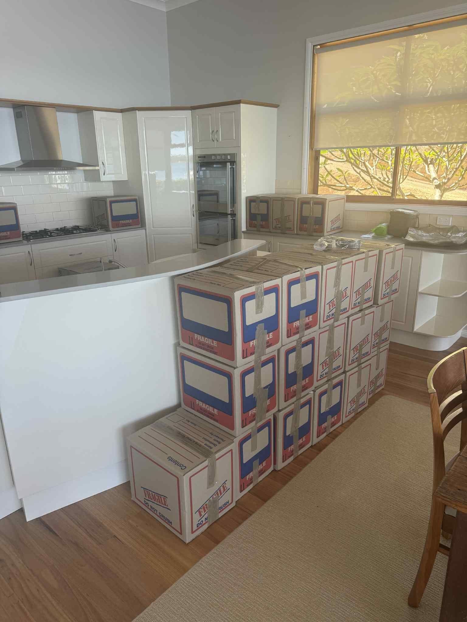 Kitchen with stacked moving boxes beside a white island and sunlit window.