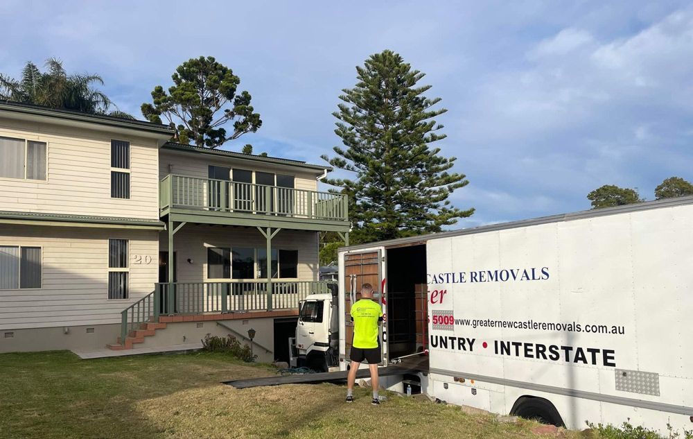Worker beside moving truck outside a beige house with a front porch and stairs