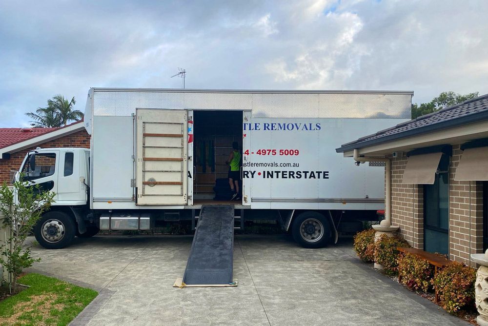 Moving truck parked in a driveway with ramp down, beside a house and garage at dusk