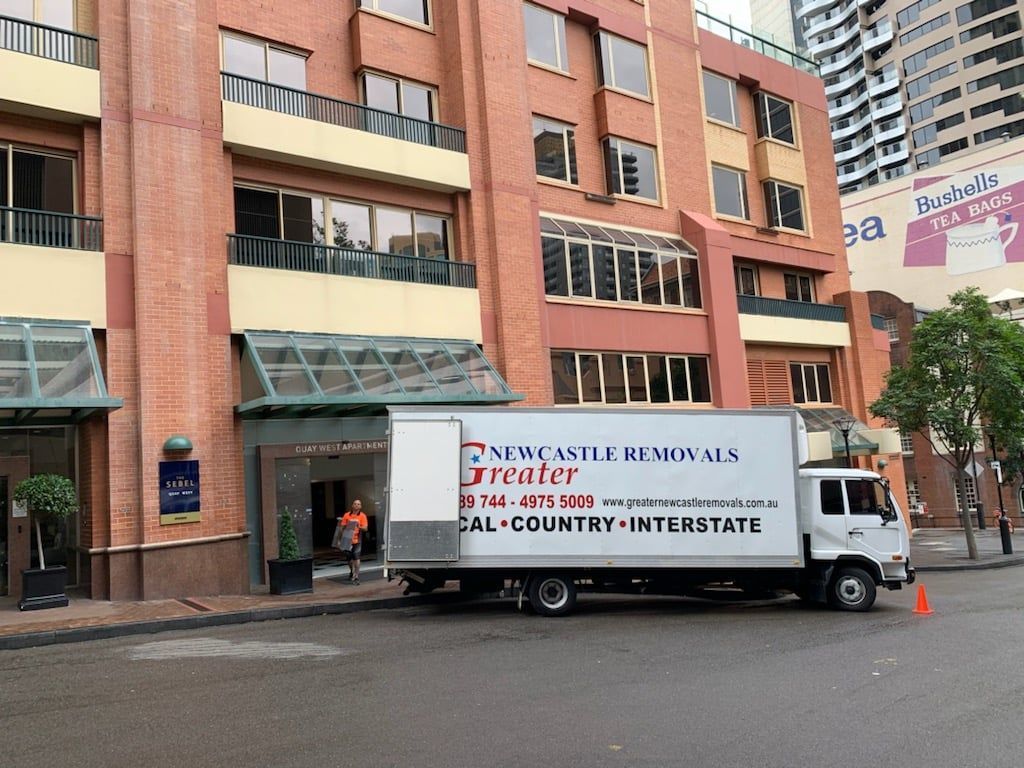 Moving truck parked outside a brick apartment building on a wet street, with a traffic cone nearby.