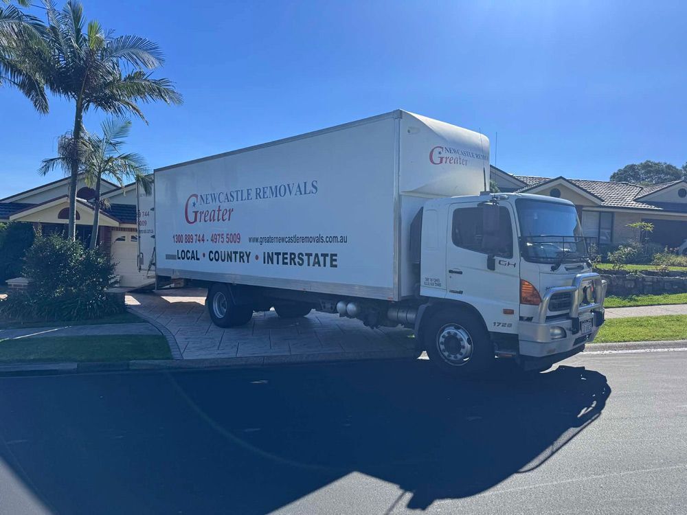 White delivery truck parked on a sunny suburban street with house and palm trees in the background