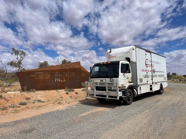 White box truck parked on a rural road beside a rusty metal container under a cloudy sky