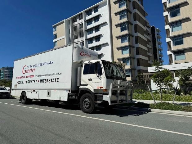 White moving truck on a sunny road beside modern apartment buildings