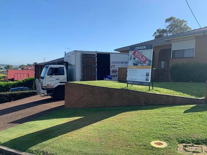 Truck parked beside brick building with a For Sale sign on a sunny lawn