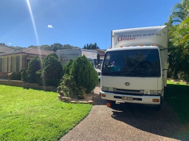White moving truck parked on a driveway beside a green lawn and house under a bright blue sky