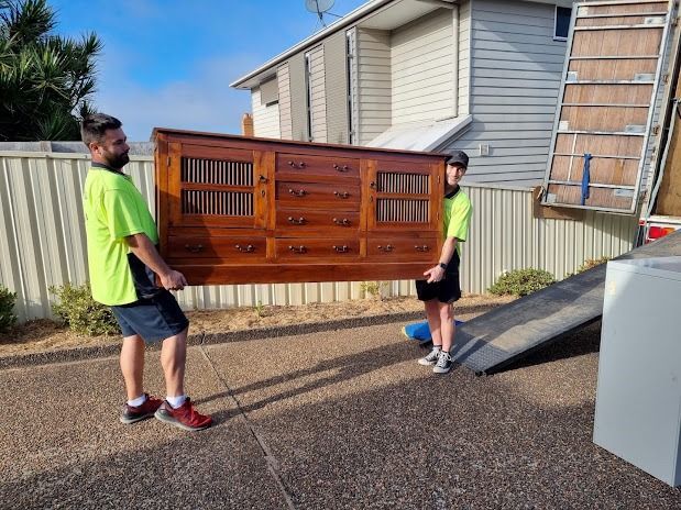 Two workers carrying a large wooden cabinet beside a moving truck in a driveway