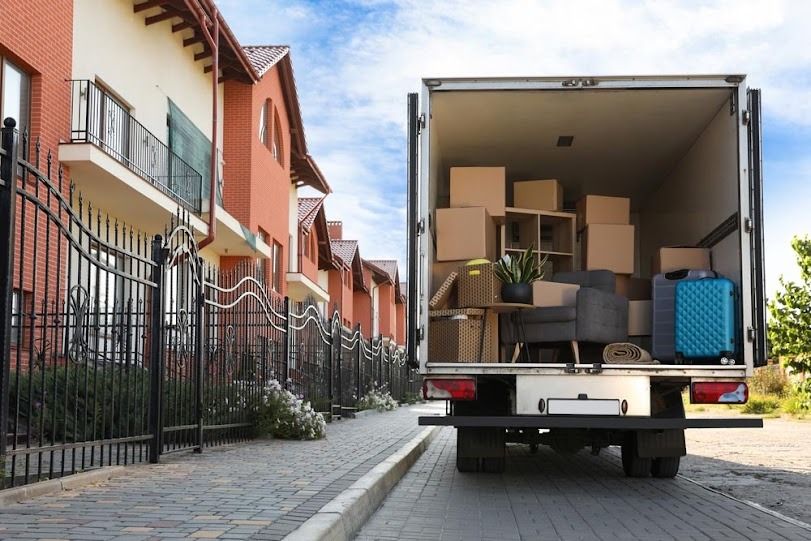 Moving truck loaded with furniture parked on a cobblestone street beside apartment buildings