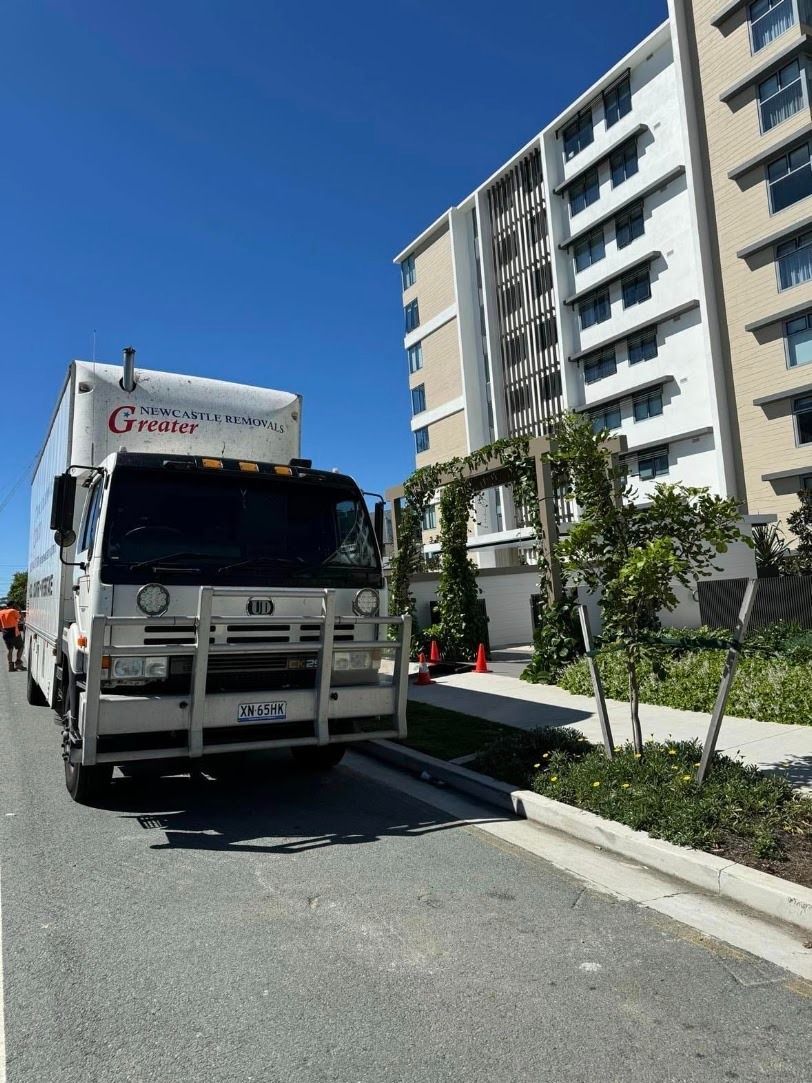 Delivery truck parked by a curb beside a white apartment building on a sunny day.