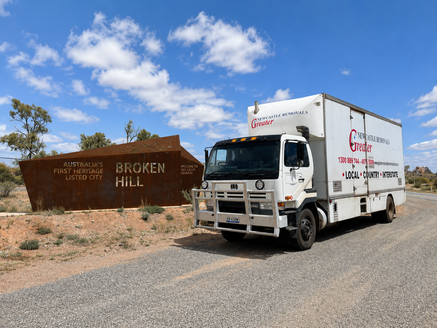 White box truck parked beside a brown sign reading “Broken Hill” under a blue sky with clouds.