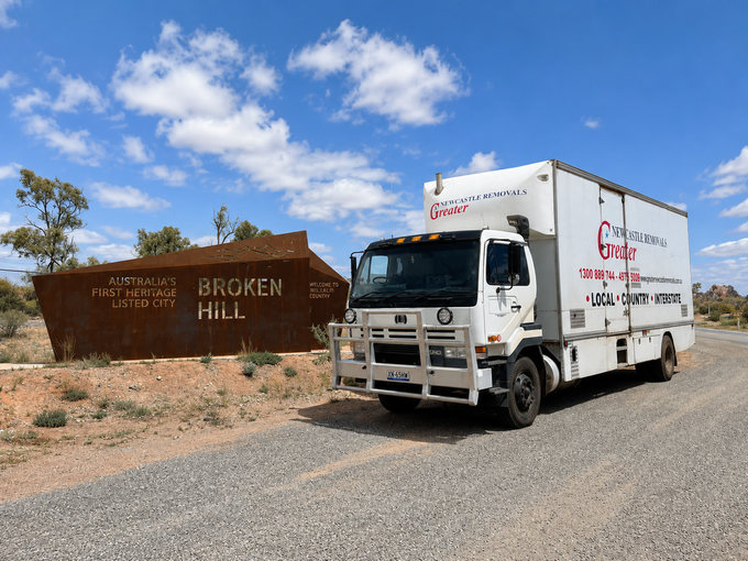 White delivery truck parked beside a brown “Broken Hill” sign under a blue sky with clouds.