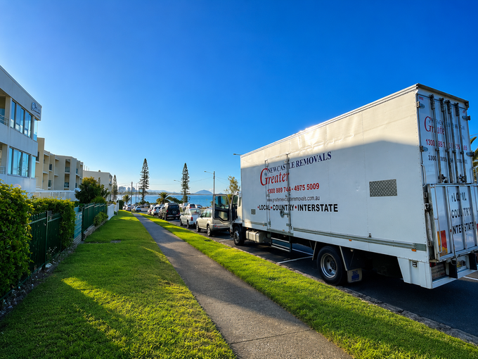 Moving truck parked along a grassy path beside apartment buildings under a bright blue sky.