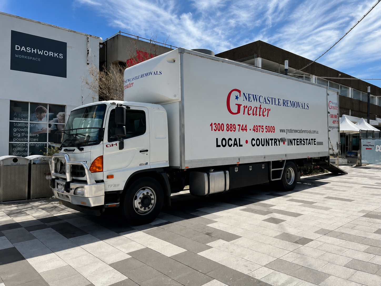 White moving truck parked outside a building under a blue sky, with commercial branding on the box side