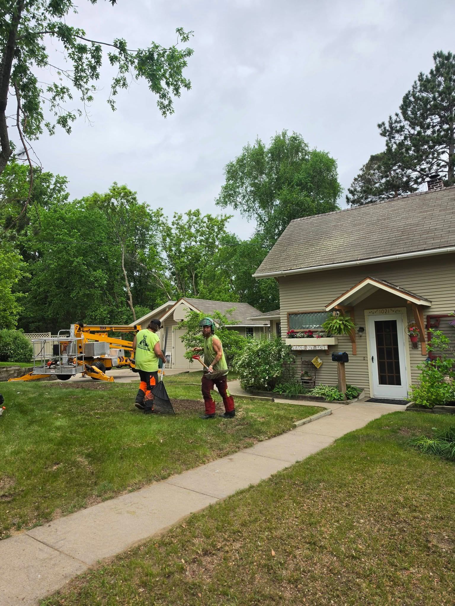 Workers in orange vests by a house and construction equipment in a grassy yard