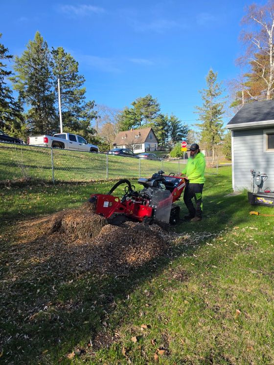 Person operating a red wood chipper in a yard beside a house on a sunny day