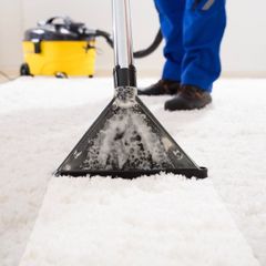 A person is using a vacuum cleaner to clean a white carpet
