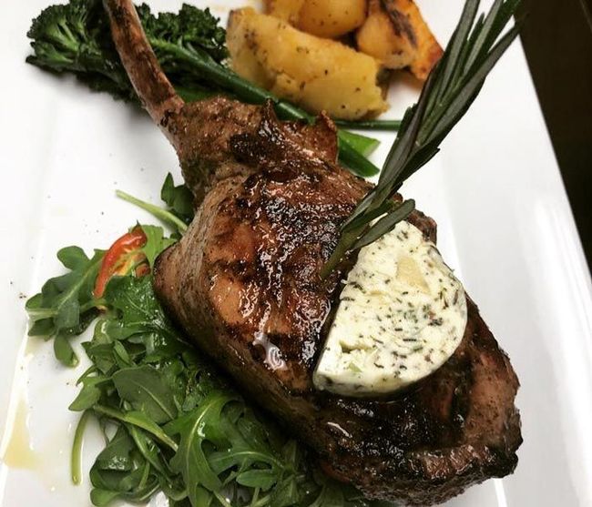 Grilled lamb chop with herb butter, roasted potatoes, and greens on a white plate