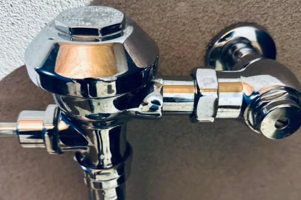 A close up of a chrome toilet flush valve on a wall