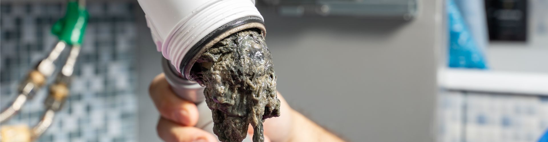 A person is holding a clogged drain filled with hair