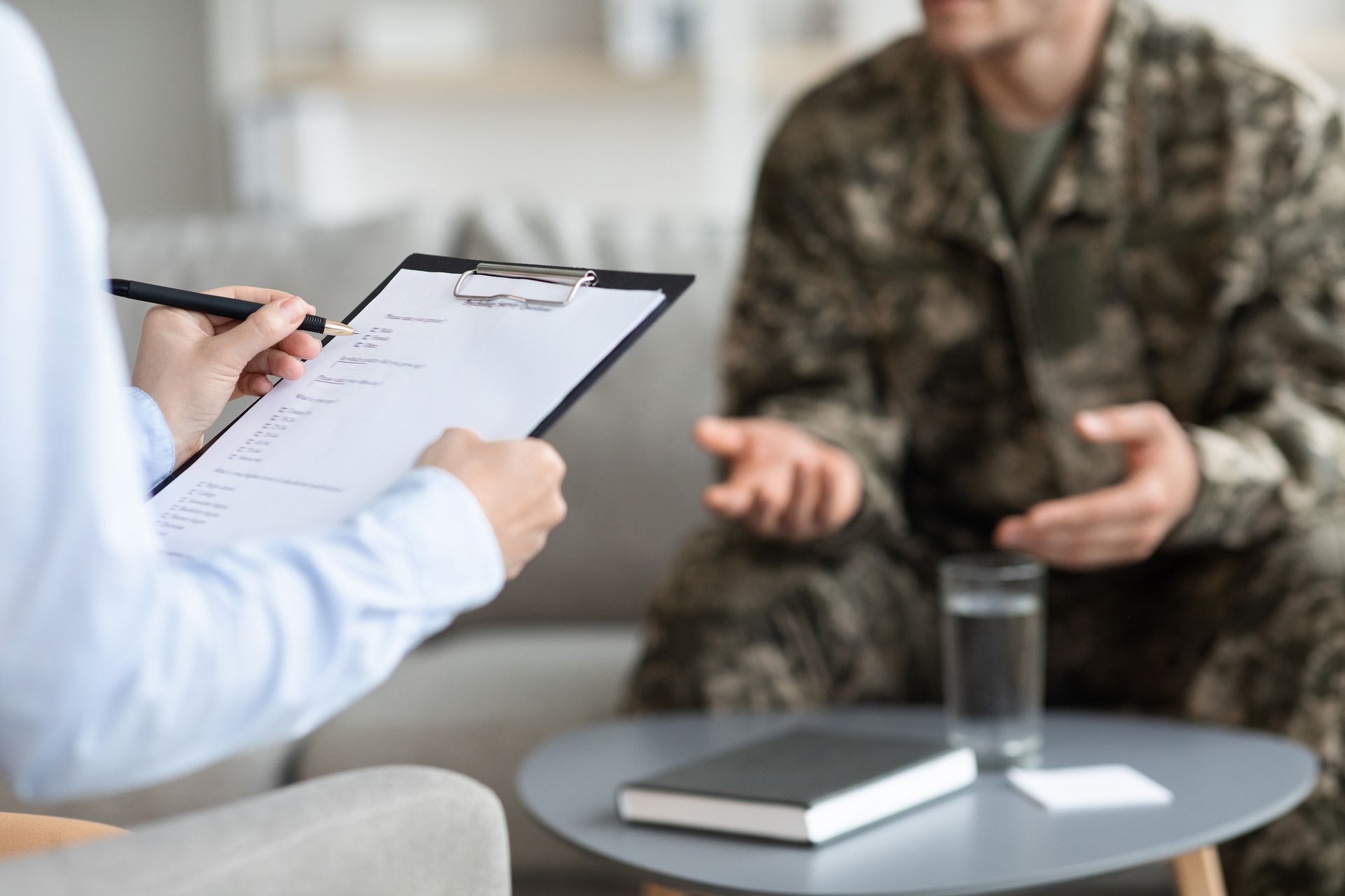 Therapist taking notes as a camouflage-clad client speaks in a counseling session