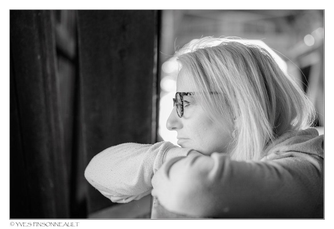 Une photo en noir et blanc d'une femme portant des lunettes regardant par la fenêtre.