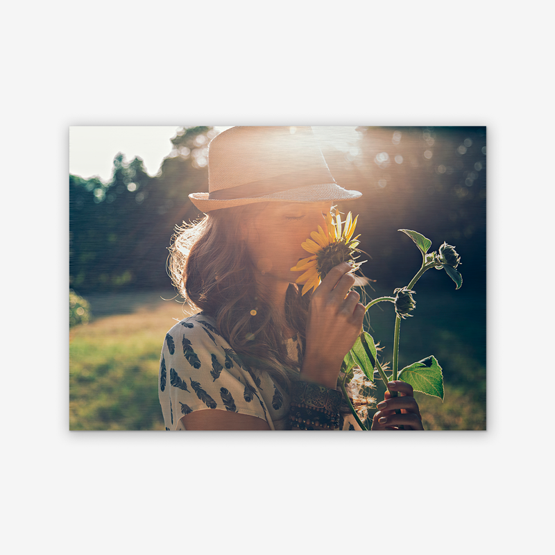 Une femme au chapeau sent un tournesol.