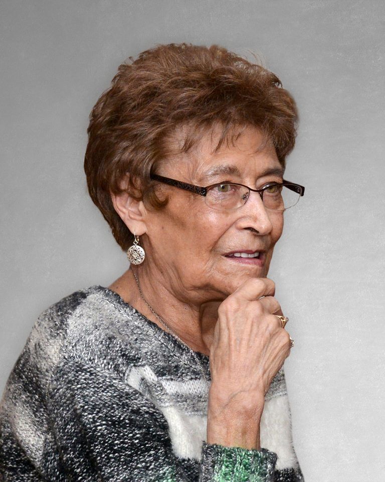 An older woman wearing glasses and earrings is holding her hand to her chin.