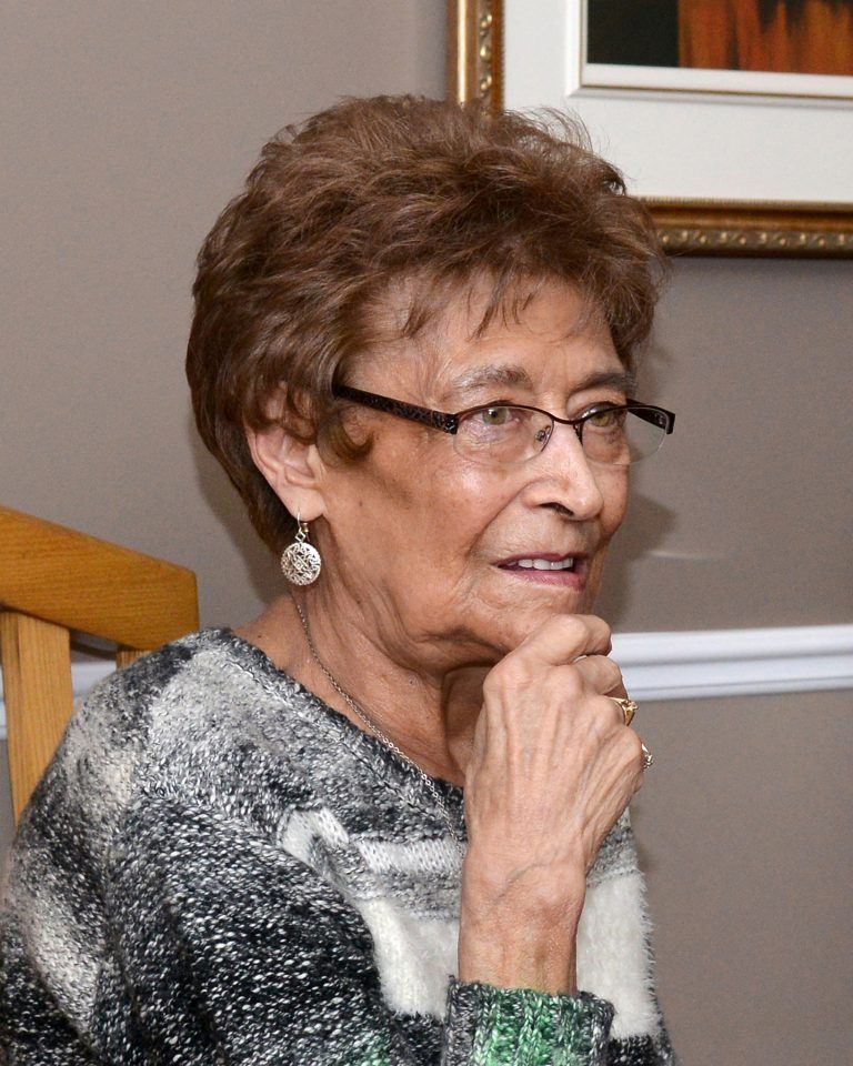 An older woman wearing glasses and earrings is sitting on a staircase.