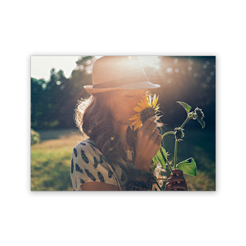 A woman in a hat is smelling a sunflower in a field.