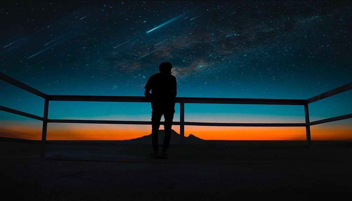 Un homme est debout sur un balcon et regarde les étoiles la nuit.