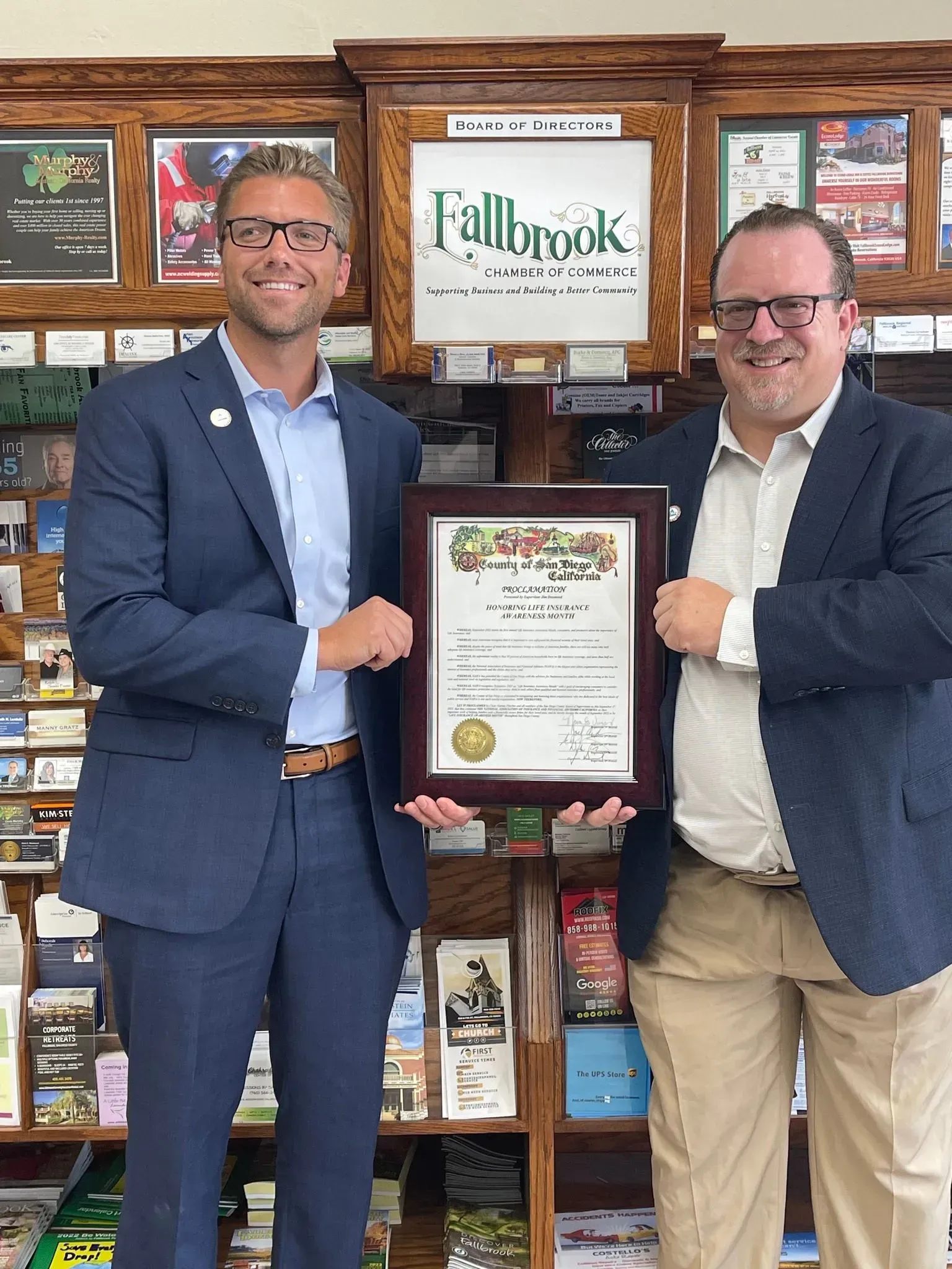 Two men in suits are standing next to each other holding a certificate.
