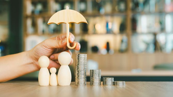 A person is holding an umbrella over a stack of coins.