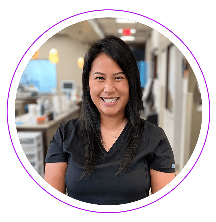 Loua L. in black scrubs smiles; blurred office background.