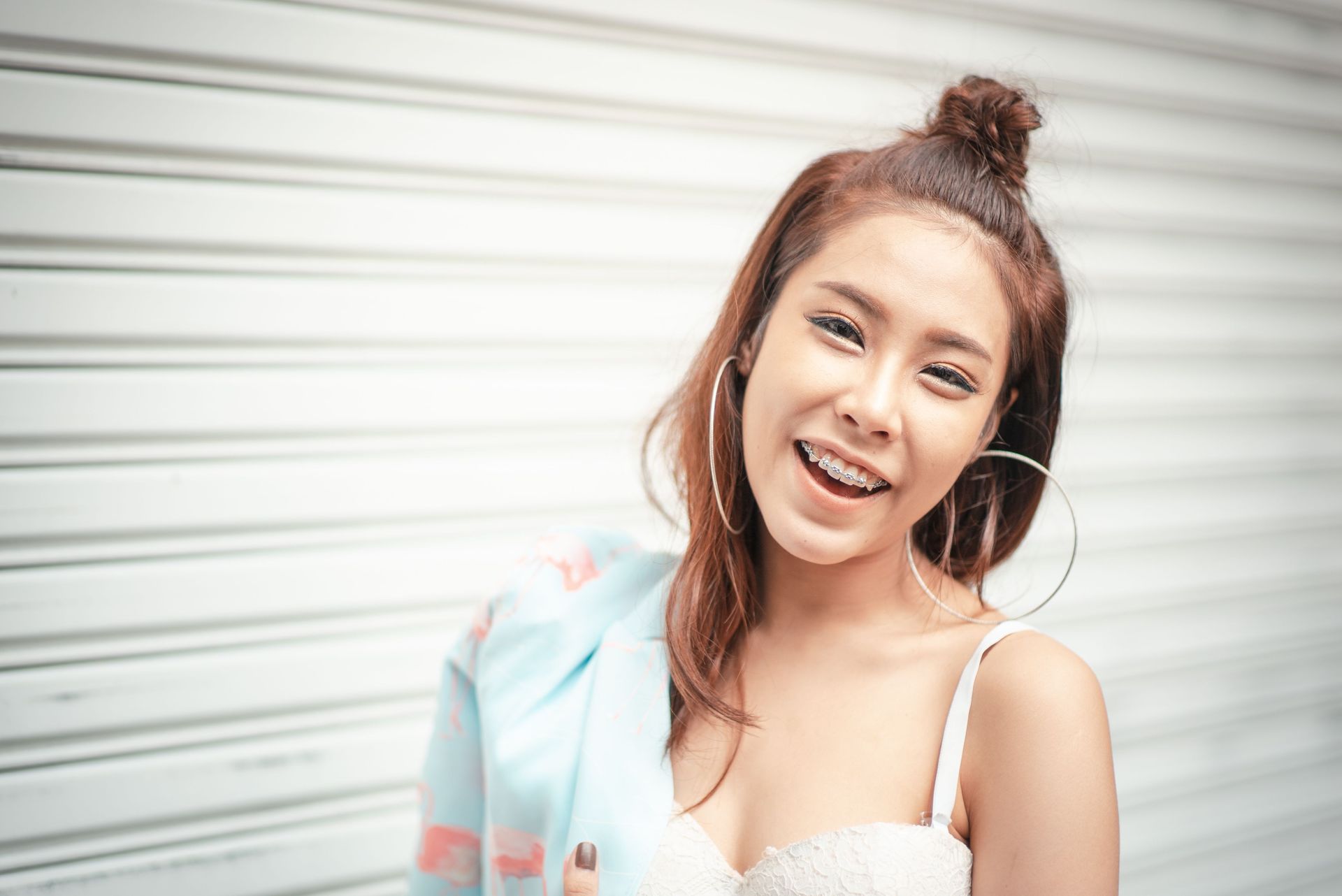 Woman with brown/red hair and big hoop earrings smiling with braces