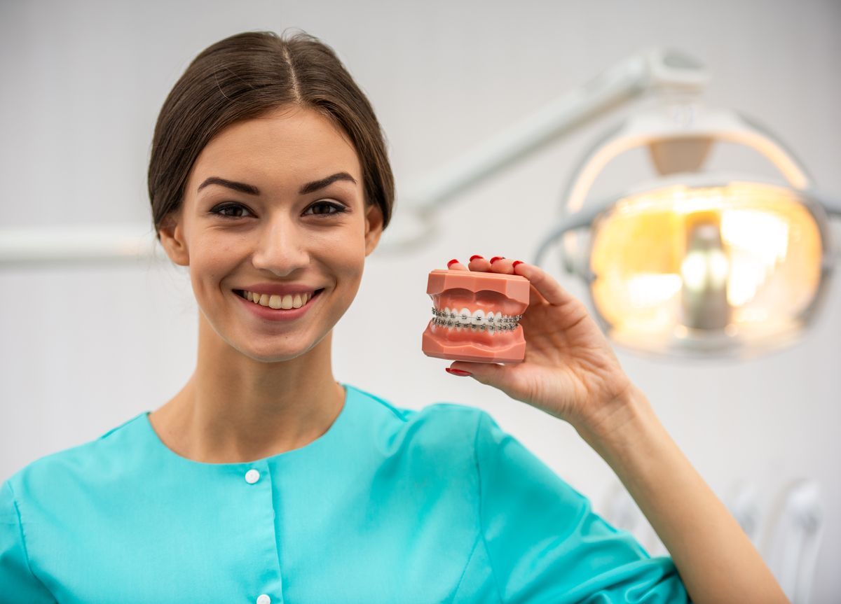 Woman in teal scrubs holding a dental model and smiling in a clinic
