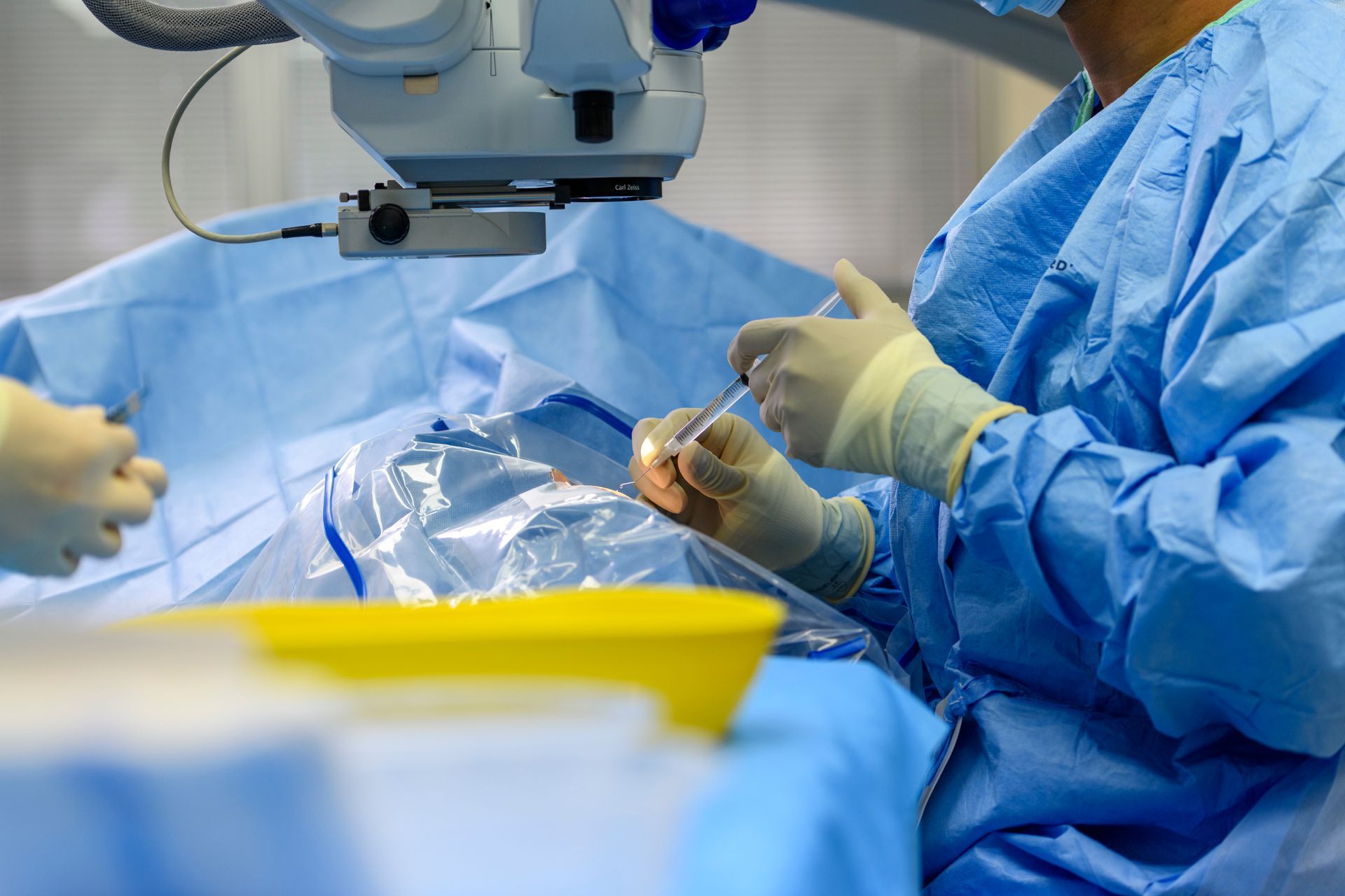 Medical staff in an operating room preparing instruments, wearing surgical attire, illuminated by overhead lights.