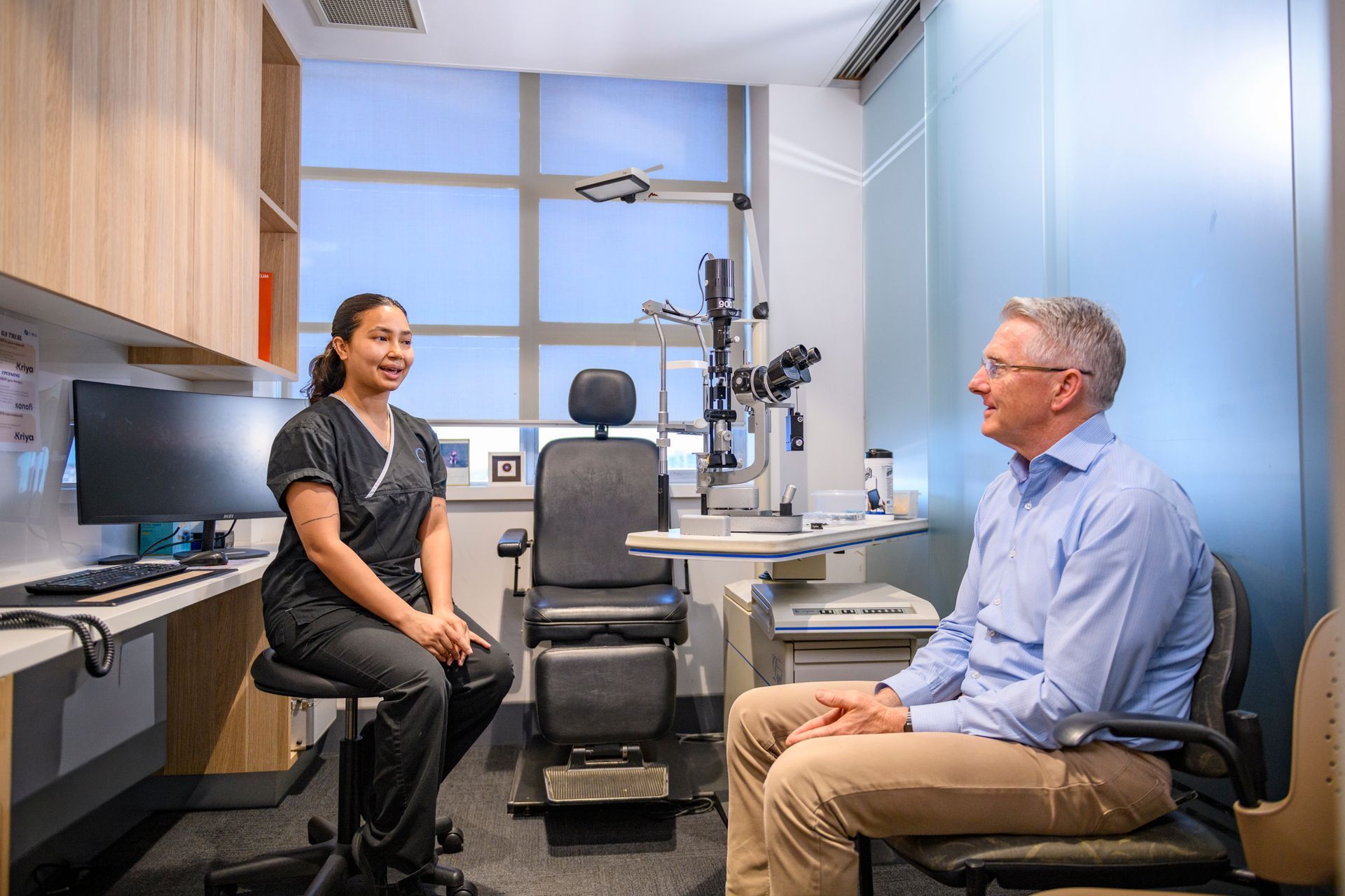 Surgeons in blue scrubs perform eye surgery using a microscope; operating room setting.