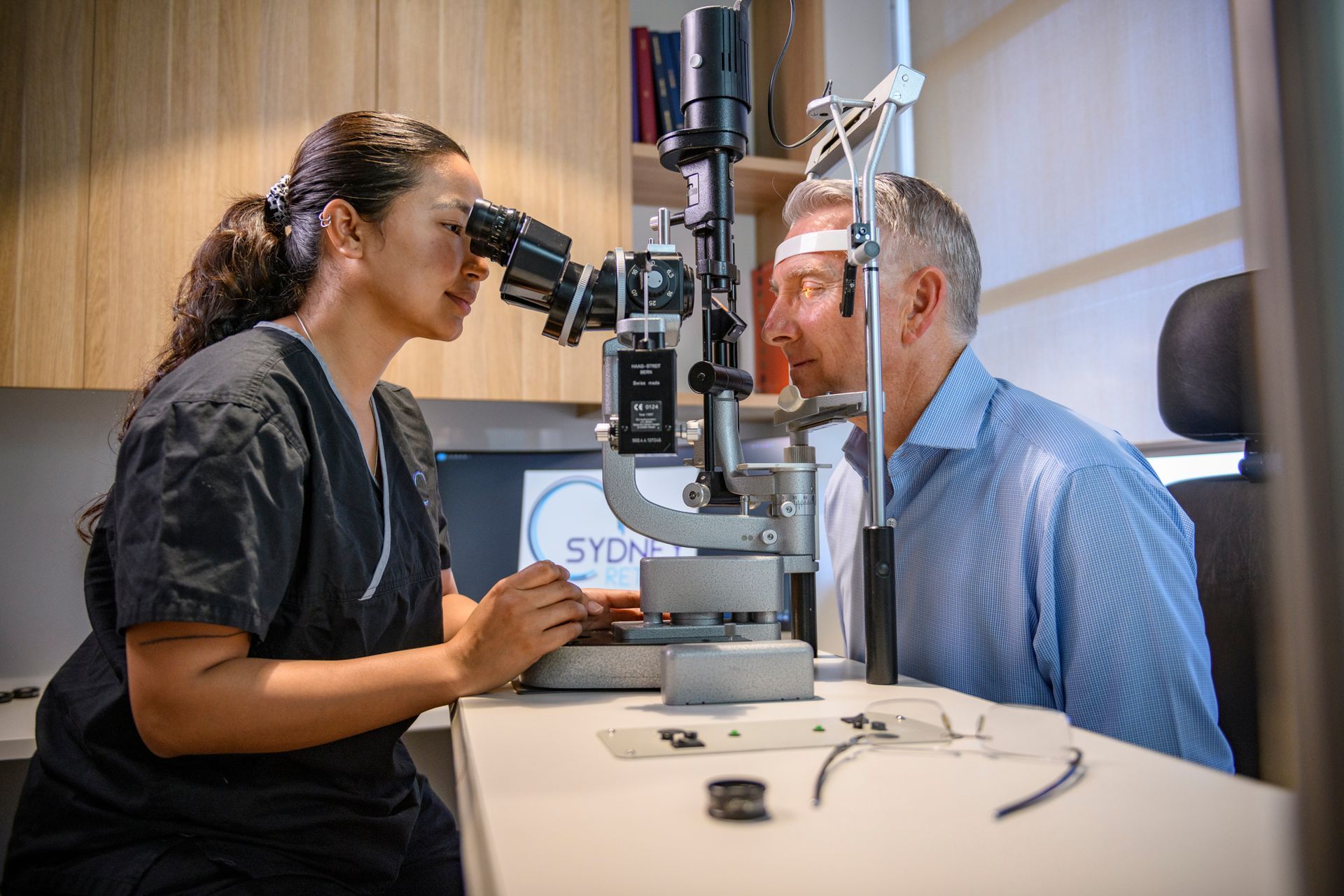 Receptionist assisting a patient at Sydney Retina clinic. White desk, TV playing, light colors.