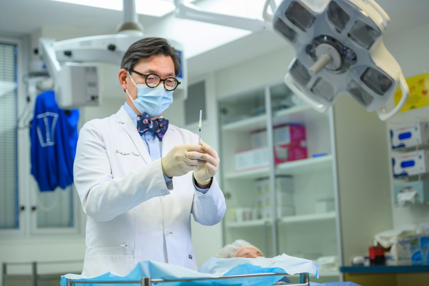 Surgeon in blue scrubs injecting a patient's eye with a needle under a microscope. Surgical setting.