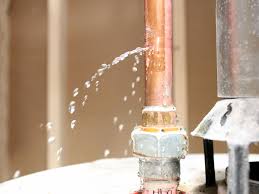 Leaking copper pipe with water spraying out, close-up shot.