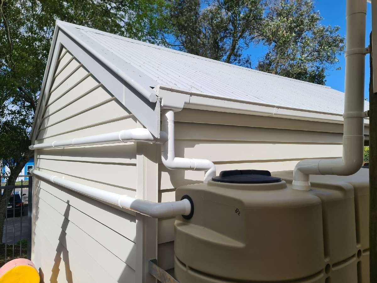 A beige water tank with white pipes attached to the side of a cream-colored building.