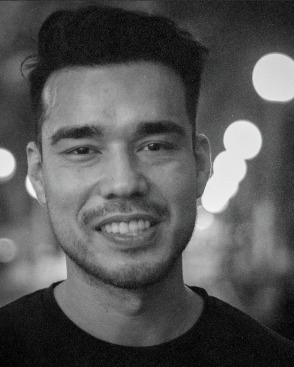 Portrait of a smiling person in a dark shirt, with blurred street lights in the background.