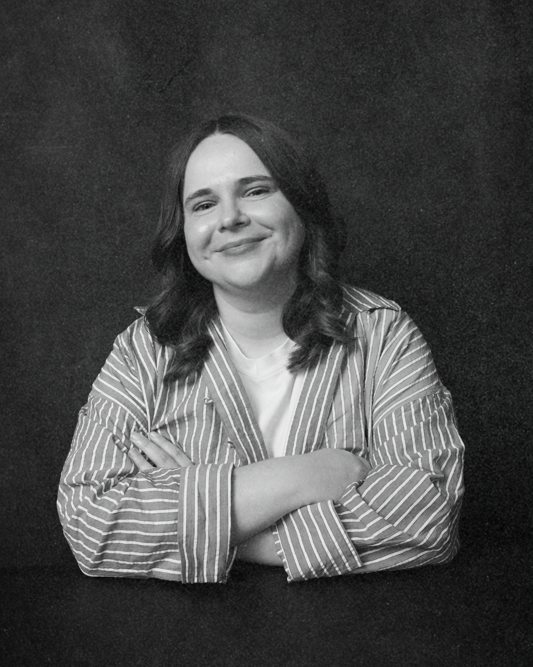 Person smiling with arms crossed, wearing a striped shirt against a plain dark background